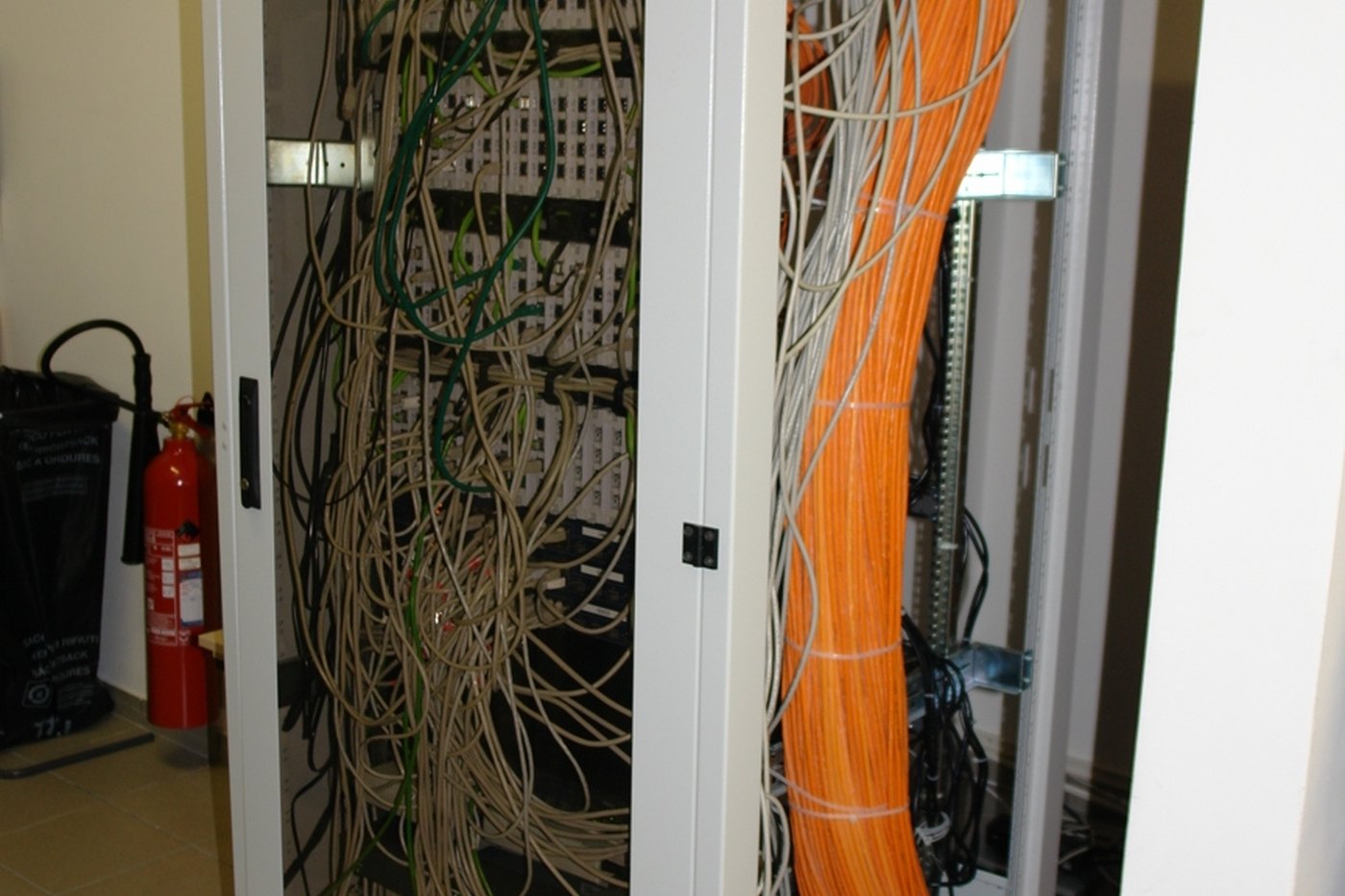 An open network rack filled with bundled patch cables and an orange fibre run