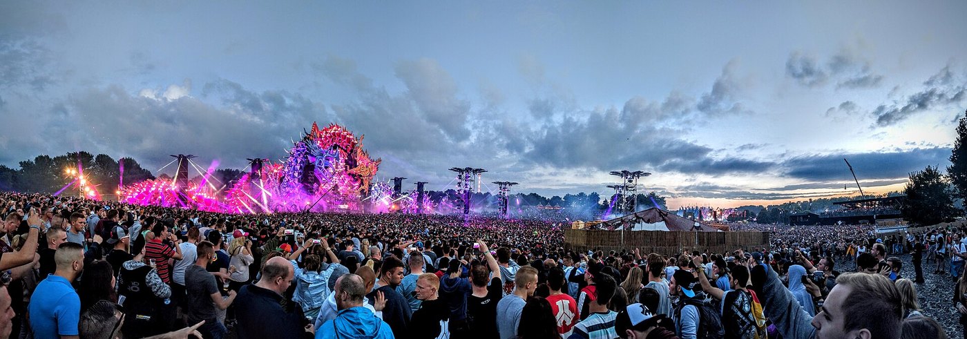 A large festival crowd standing in front of a lit stage at dusk